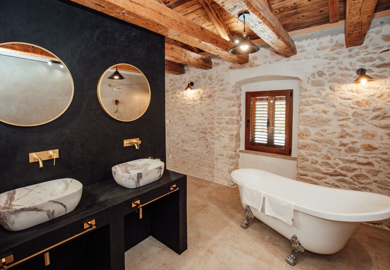 Upper-floor en-suite bathroom with double washbasin, bathtub and stone wall.
