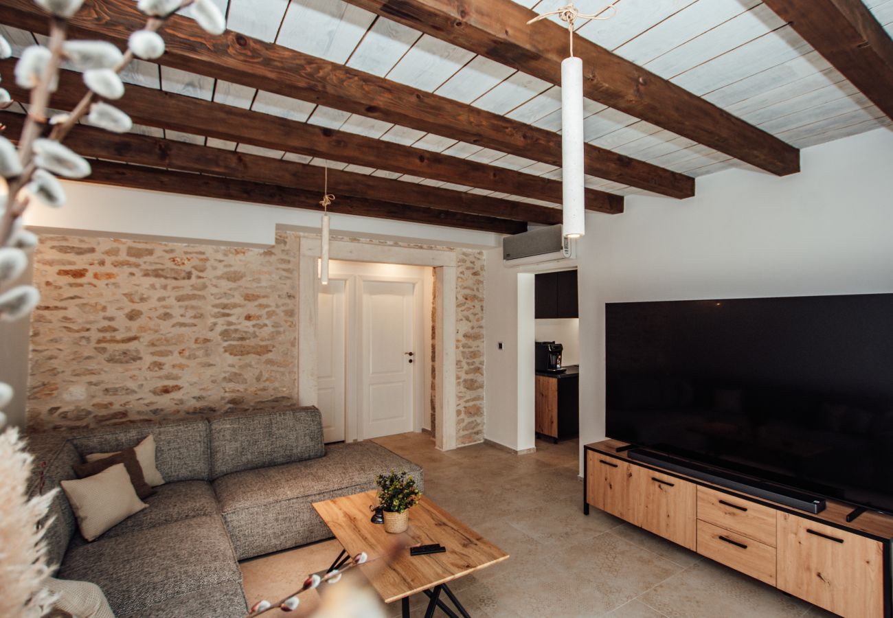 Living room of Gland Residence in Nin with seating area, Smart TV, stone wall and wooden beam ceiling.