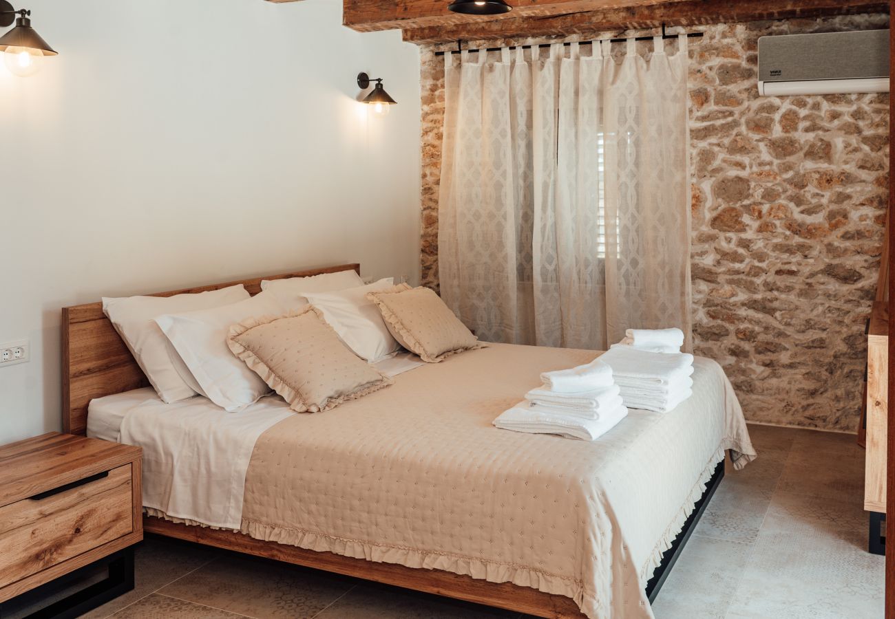 Upper-floor bedroom of Gland Residence in Nin with king-size double bed, air conditioning and stone wall