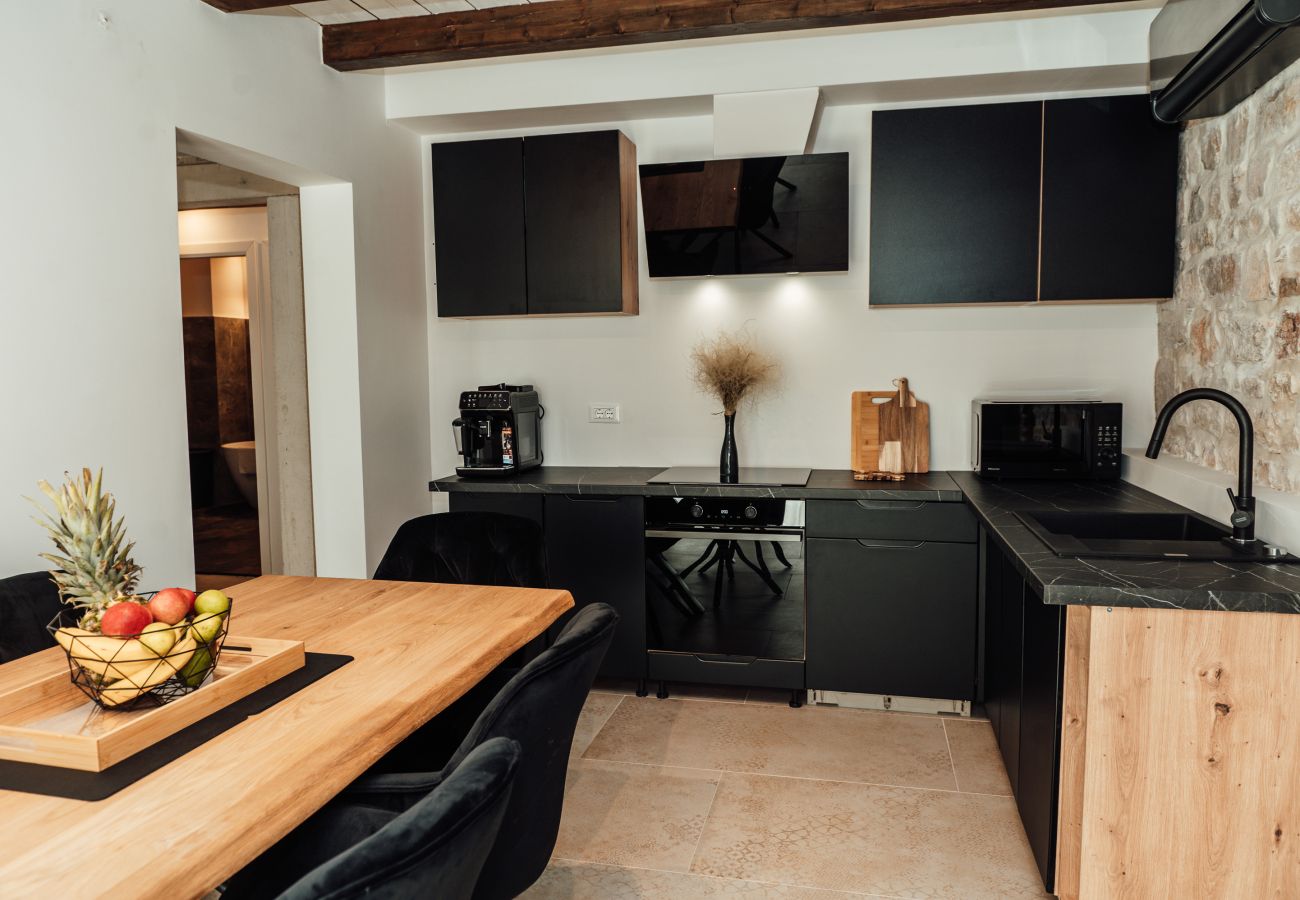 Separate kitchen of Gland Residence in Nin with dining area, modern appliances and stone wall.