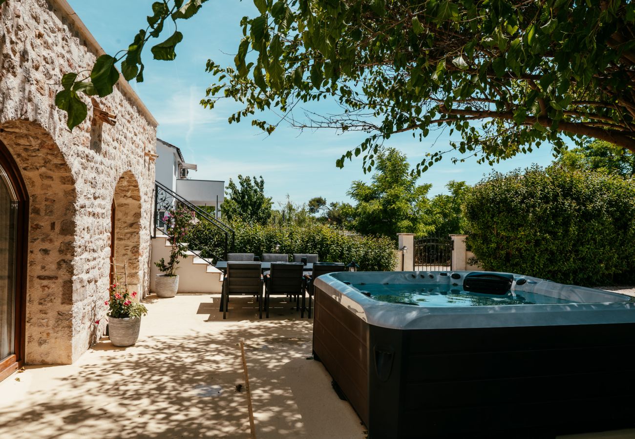 Private garden area of Gland Residence in Nin with whirlpool, outdoor dining space and stone façade.
