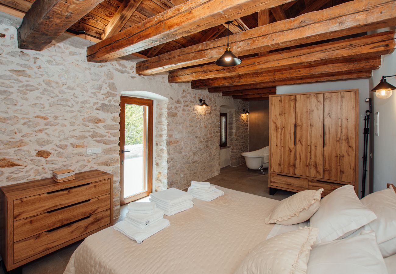 Schlafzimmer im Obergeschoss mit Kingsize-Bett, Natursteinwand und en-suite Badbereich.