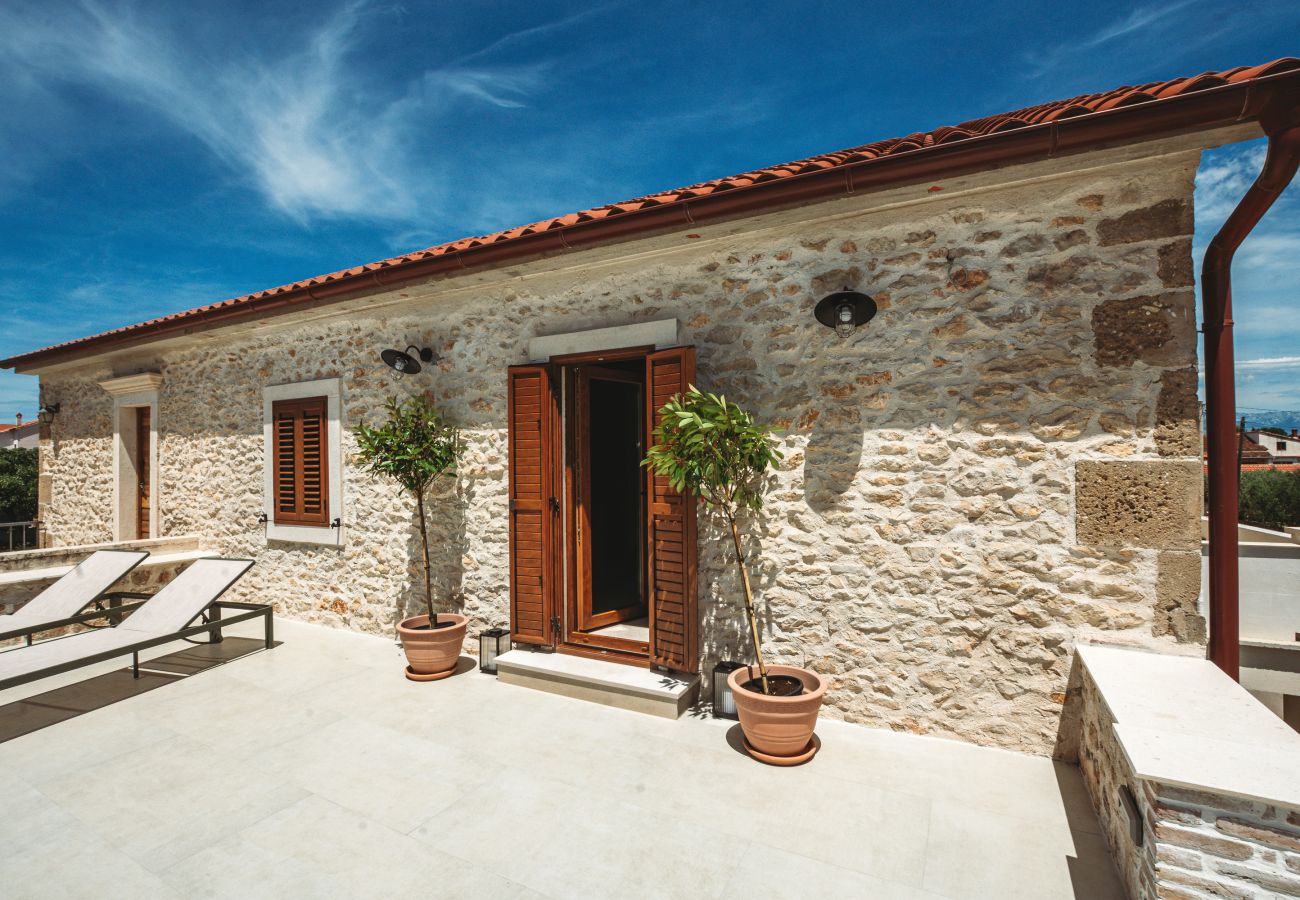 Obere Sonnenterrasse der Gland Residence in Nin mit Sonnenliegen und Natursteinfassade.